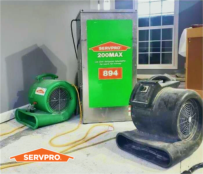 a group of drying pieces of equipment with SERVPRO logos, green air mover and HEPA filter dehumidifier on a floor in a house